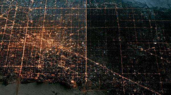 Aerial satellite view of city with half lit and half in complete darkness during rolling blackout