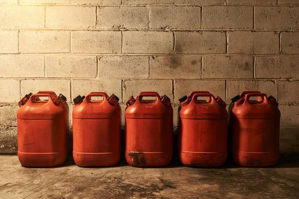 Five red plastic gasoline cans lined up against a concrete block wall in a garage