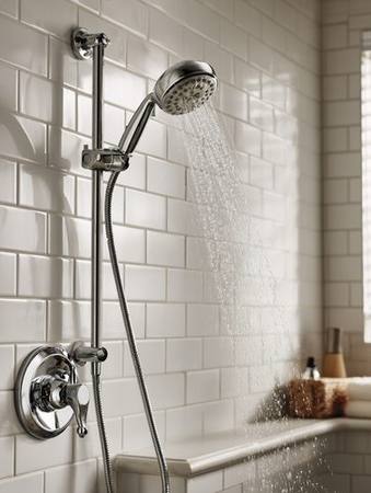 Chrome handheld showerhead on adjustable sliding bar running water in white tiled shower